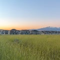 Square Vast terrain with green grasses against houses mountain and blue sky at sunset