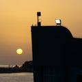 Yellow sun over the horizon at sunset, building silhouette in first plan with a spotlight at the top, Madeira island, Portugal.