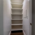 Square Walk in closet or pantry with empty wall shelves seen through open hinged door