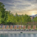 Square Whispy white clouds Lounge chairs on a public pool with wired fence at Daybreak, Uta
