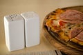 Square white jars of salt and pepper stand on table next to a thin fresh delicious pizza Royalty Free Stock Photo