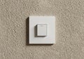 A square, white light switch is mounted on a textured beige wall. The switch plate Royalty Free Stock Photo