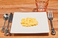 Square, white plate of freshly prepared, scrambled eggs, with a set of artisan utensils, empty, pink glass