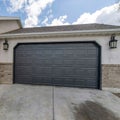 Square White puffy clouds Clipped corner black sectional garage door exterior with a concrete driveway Royalty Free Stock Photo