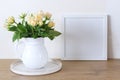 Square wooden frame mockup on a vintage bench, table. Modern white ceramic vase with white roses. White wall background. Royalty Free Stock Photo