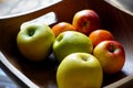 Square wooden fruit bowl containing imperfect red and green apples, and oranges Royalty Free Stock Photo