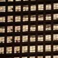 Squared image of a window with people working in the interior of an office building at night.