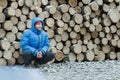 Squatting lumberjack at stack of logged firewood background outdoors in winter mountain forest Royalty Free Stock Photo