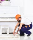 Squatting man in orange protective helmet preparing flat for redecoration. Side view guy rolling white carpet Royalty Free Stock Photo