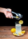 Squeezing lemon into a glass of lemonade with yellow lemons around a white plate Royalty Free Stock Photo