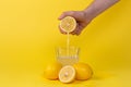 Squeezing lemon juice into glass on yellow background Royalty Free Stock Photo