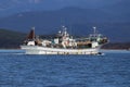 Squid fishing boat underway at sea on background of green coastal mountains. Fishing schooner equipped with lights to catch squid Royalty Free Stock Photo