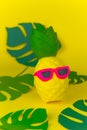 pineapple in sunglasses on yellow background among paper cut tropical leaves