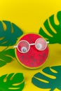 watermelon in glasses on yellow background among paper cut tropical leaves