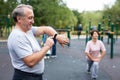 Ssenior man in sportswear looks at fitness watch or at pedometer while exercising in city park