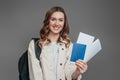 sstudy abroad concept. student girl holding backpack, book, notebook, passport isolated on a dark grey background
