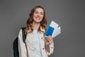 sstudy abroad concept. student girl holding backpack, book, notebook, passport isolated on a dark grey background