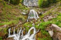 St. Beatus Cave and waterfalls above Thunersee, Sundlauenen, Switzerland. Falls are running down the mountain with a green grass