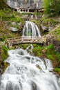 St. Beatus Cave and waterfalls above Thunersee, Sundlauenen, Switzerland. Falls are running down the mountain with a green grass