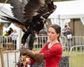 Wedge tailed eagle with wings outstretched, standing on gloved hand of female trainer / handler in red dress, getting ready for