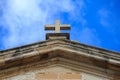 St John Baptist chapel in Malta. White cross on the top of a limestone building. Blue sky with clouds background.