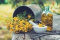 St Johns wort flowers, oil or infusion bottle, mortar and big vintage metal mug of Hypericum plants on wooden board.