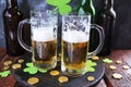 St. Patrick`s Day, fresh beer in glass mugs and a bottle, gold coins, on a red wooden table, a green shamrock on a dark background Royalty Free Stock Photo