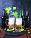 St. Patrick`s Day, fresh beer in glass mugs and a bottle, gold coins, on a red wooden table, a green shamrock on a dark background Royalty Free Stock Photo