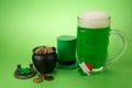 St Patrick`s Day green beer with shamrock, pot with gold coins, horseshoe and Leprechaun hat against green background.