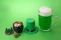 St Patrick`s Day green beer with shamrock, pot with gold coins, horseshoe and Leprechaun hat against green background.
