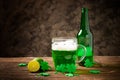 St. Patrick`s Day, green shamrock with a full cold glass of traditional green beer and foam on a wooden background