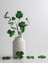 St. PatrickÃ¢â¬â¢s Day green swirls, four leaf clovers and a hat in a white vase with more glittery green four leaf clovers on a