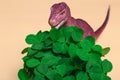 St. Patrick\'s Day happy dinosaur, a bouquet of clover in a bucket and gold coins on a beige background. Closeup copy space