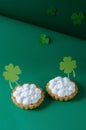 St. Patrick`s Day. Two tarts with cream and decorative craft paper shamrocks on a green background