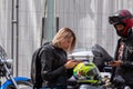 Girl motorcyclist sitting on a motorcycle looking at a smartphone. Nearby is a man in a helmet with a phone in his hand