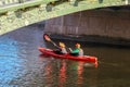 A man and a woman row in a red kayak on the river under the bridge. Kayaking in the city