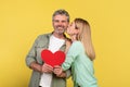 St. Valentines day concept. Loving mature spouses holding red paper heart card, woman kissing her happy husband Royalty Free Stock Photo