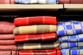 A stack of beautiful woolen blankets in red, blue, yellow, pink. A pile of soft warm blankets in store. Close up. Things for home