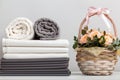A stack of bed linen, rolls of white and gray towels. Basket with roses on the table