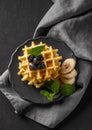 A stack of belgian waffles with kiwi, banana slices and mint, drizzled with honey syrup on a gray plate on a dark background close Royalty Free Stock Photo