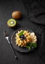 A stack of belgian waffles with kiwi, banana slices and mint, drizzled with honey syrup on a gray plate on a dark background Royalty Free Stock Photo