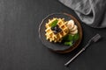 A stack of belgian waffles with kiwi, banana slices and mint, drizzled with honey syrup on a gray plate on a dark background Royalty Free Stock Photo