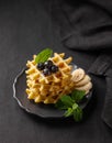 A stack of belgian waffles with kiwi, banana slices and mint, drizzled with honey syrup on a gray plate on a dark background with Royalty Free Stock Photo