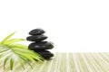 Stack of black basalt balancing stones with green leaf on bamboo mat, on white background.