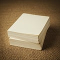 Stack of blank, square paper sheets on a textured burlap surface. The paper has a Royalty Free Stock Photo