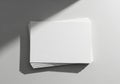 A stack of blank white paper lies on a smooth gray surface, partially illuminated by light Royalty Free Stock Photo