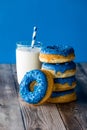A stack of blue chocolate candy dipped donuts with a glass of milk.
