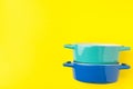 Stack of blue and turquoise ceramic cocottes on bright yellow background. Cooking baking cookware concept