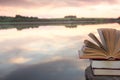 Stack of book and Open hardback book on blurred nature landscape backdrop against sunset sky with back light. Copy space, back to Royalty Free Stock Photo