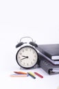 Stack of book with ticking vintage clock and colorful crayon on white table